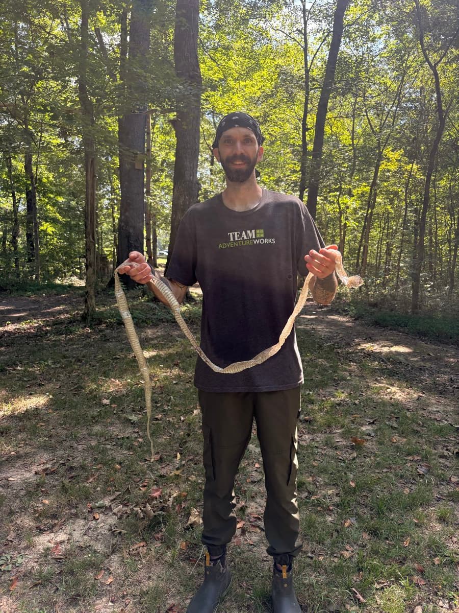 Guide in a Team Adventureworks shirt holding up a shed snake skin in the forest