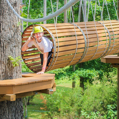 Young man navigating a fun tunnel section of a ropes course adventure
