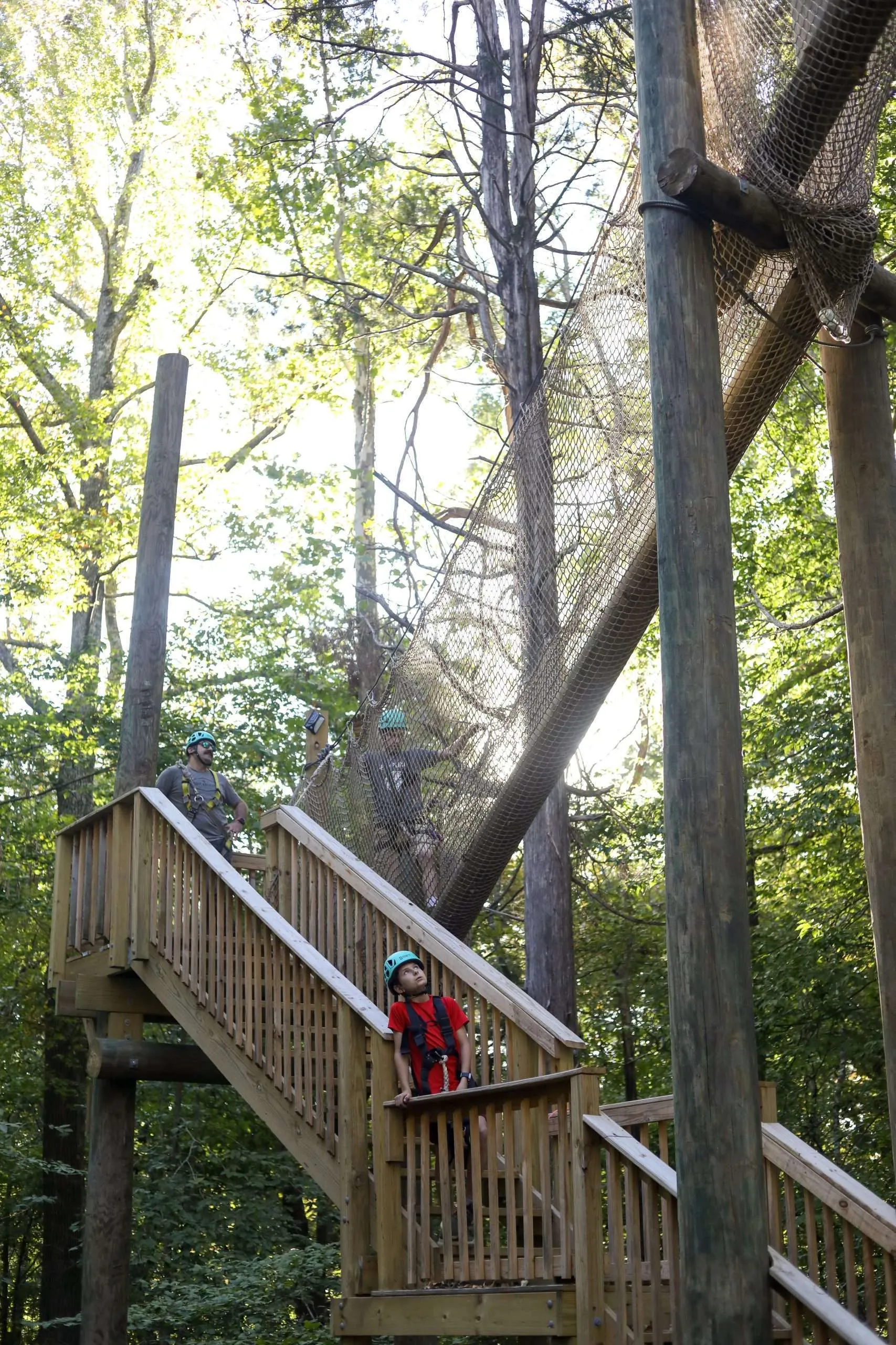 Child wearing a helmet and harness looking up from a zipline platform on a treetop adventure course in Tennessee